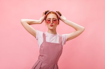 lovely-woman-with-buns-dressed-pink-overalls-white-t-shirt-posing-with-closed-eyes-pink-background