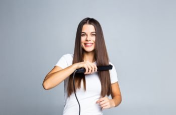 portrait-cheerful-woman-using-straightener-her-curly-hair-preparing-event-date-holiday-comfortable-easy-hairdo-isolated-grey